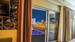 Una habitación de hotel moderna con un amplio ventanal corredero que da a un balcón con vistas a la ciudad.