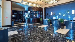 Un moderno vestíbulo de hotel con piso de mármol, mostradores de recepción y arte decorativo en las paredes.