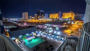 Zona de piscina en la azotea con sillones de descanso y una piscina, rodeada de edificios altos con ventanas iluminadas.