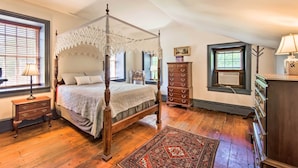 Een hemelbed met gordijnen, een dressoir, een nachtkastje en een raam met zonwering.