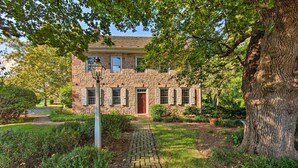 Een stenen huis met een pad van baksteen dat naar de ingang leidt, omringd door groen en bomen.
