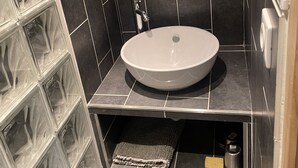 A bathroom with a round sink, dark tiled walls, a mirror, and a towel rack. - Apartment at the foot of the slopes (Morzine)