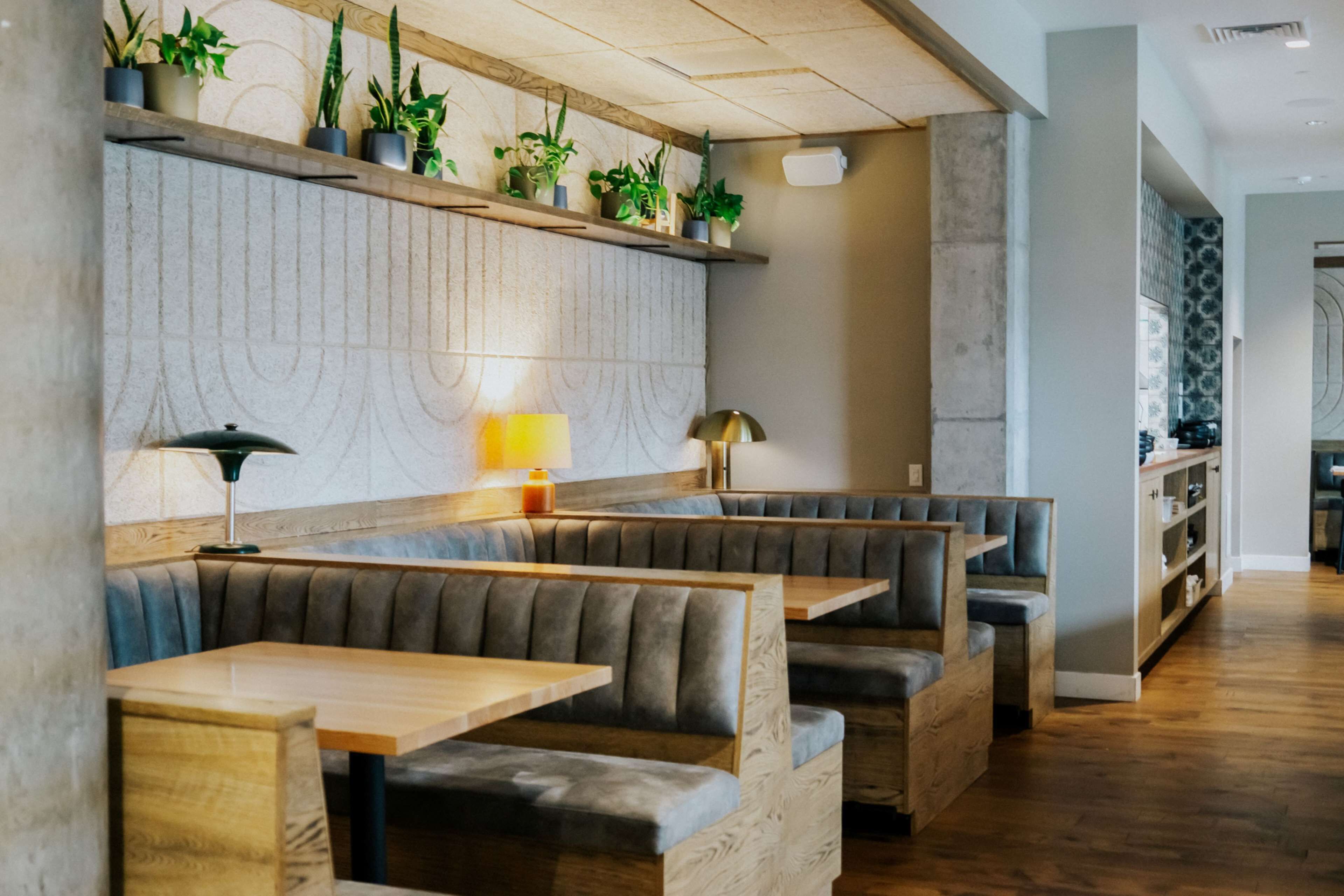 Een restaurant met houten tafels en comfortabele zitbanken, een stenen muur met een reliëf patroon, en schappen met potplanten.