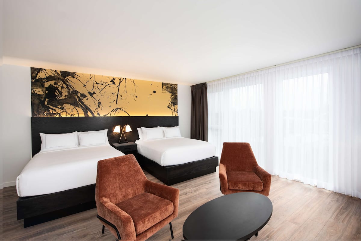 Ein Hotelzimmer mit einem großen Bett, zwei Sesseln, einem kleinen Tisch und einem Wandbild.
