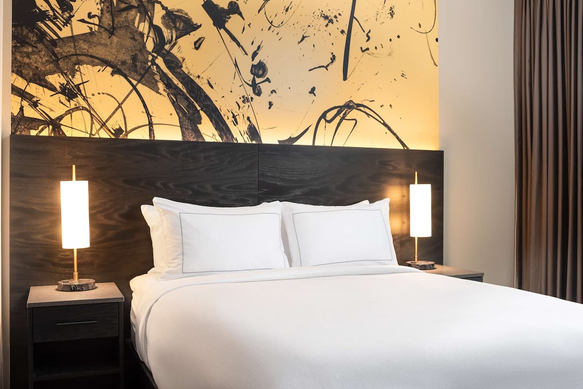 Ein Hotelzimmer mit einem großen Bett, zwei Nachttischen und einer Wand mit abstrakter Kunst.