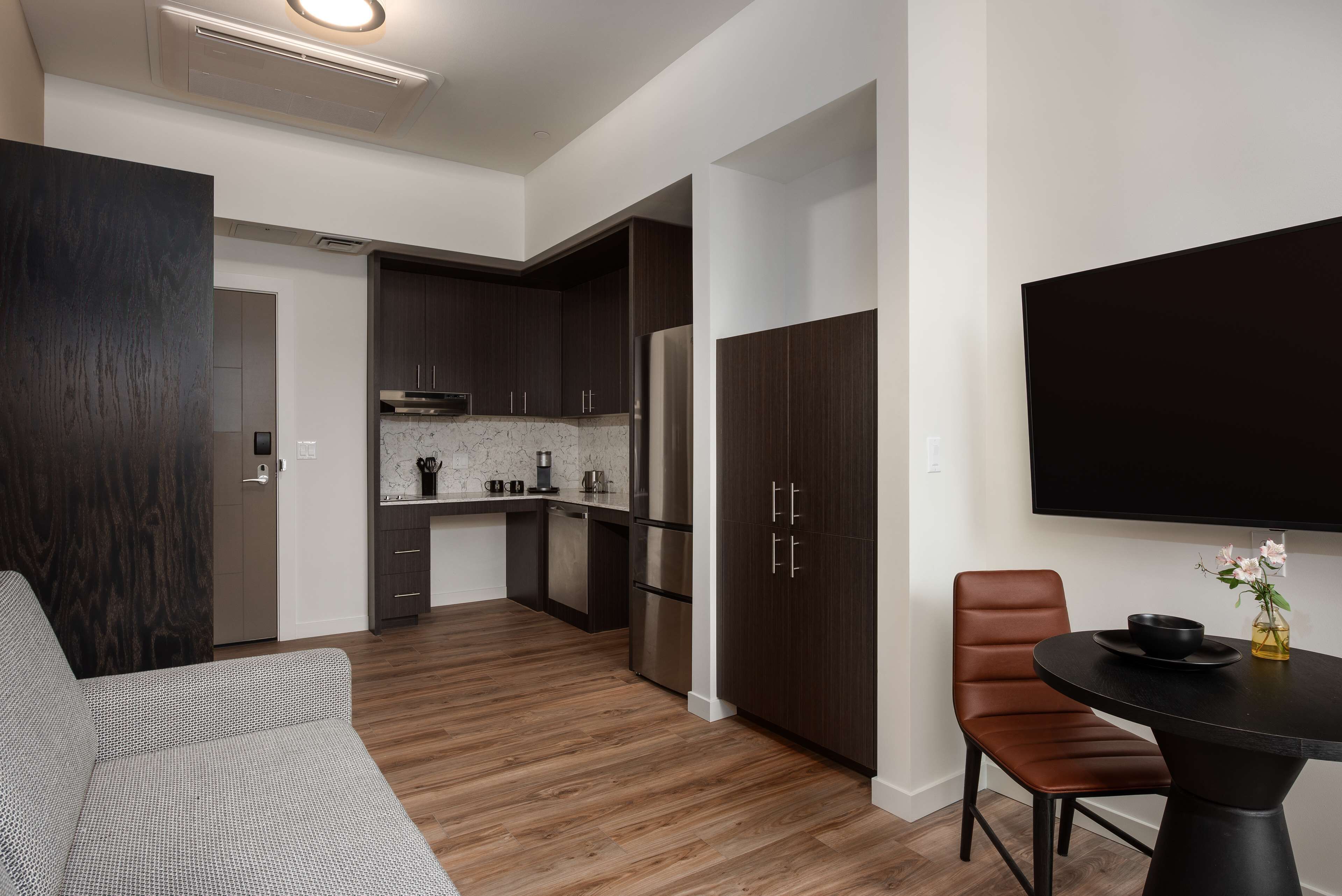 A modern kitchen with dark cabinets, a stainless steel refrigerator, and a marble countertop.