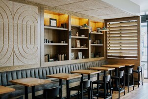 A modern restaurant interior with wooden shelves, a cushioned bench, and wooden tables.