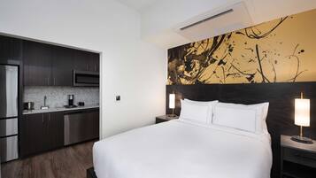 Una habitación de hotel moderna con una cama grande, una kitchenette y una original obra de arte abstracta en la pared.