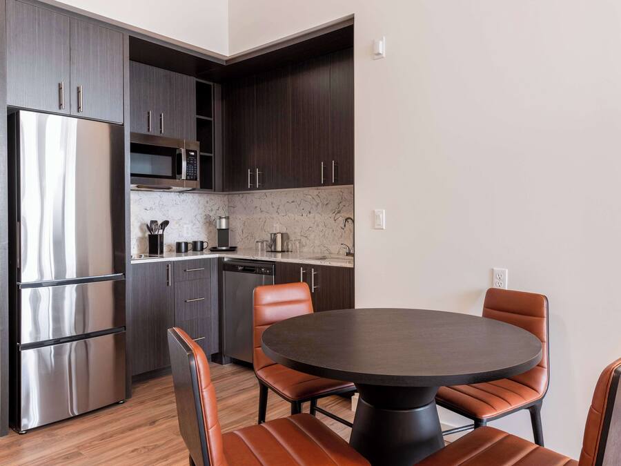 Una cocina moderna con armarios oscuros, electrodomésticos de acero inoxidable y una mesa redonda con sillas de cuero.