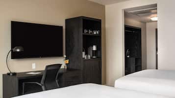 Een hotelkamer met een bed, een bureau met stoel, een aan de muur bevestigde televisie, een kledingkast en een plank met keukenbenodigdheden.