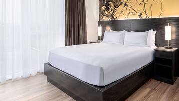 Quarto de hotel moderno com uma cama grande, cabeceira de madeira escura, roupa de cama branca e um quadro na parede.