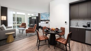 A modern hotel room with a dining area, a sofa, a TV, and a kitchen area. - Holman Riverfront Park Hotel Salem, Tapestry by Hilton (Salem)