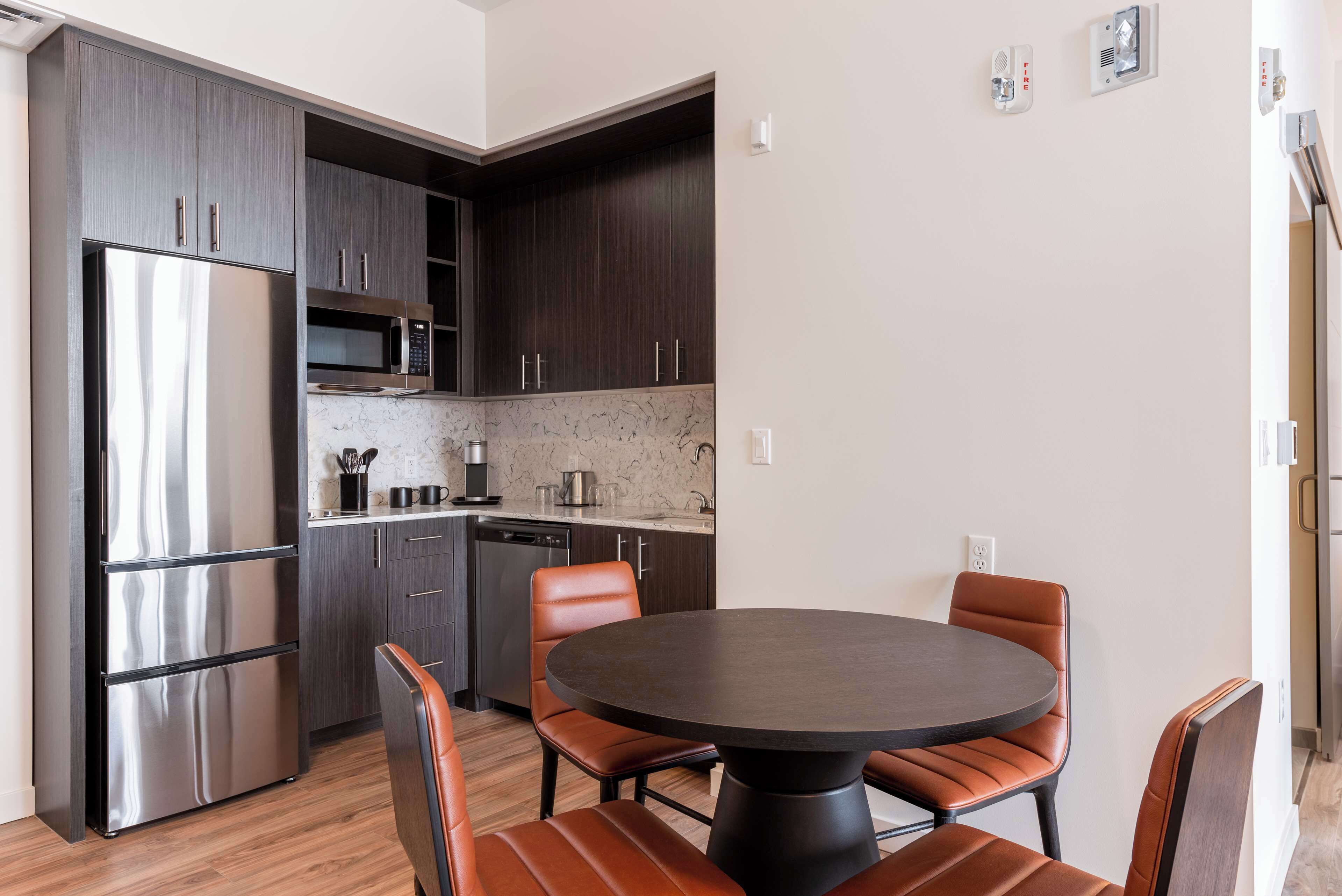 A modern kitchen with dark cabinets, stainless steel appliances, and a round dining table with leather chairs.