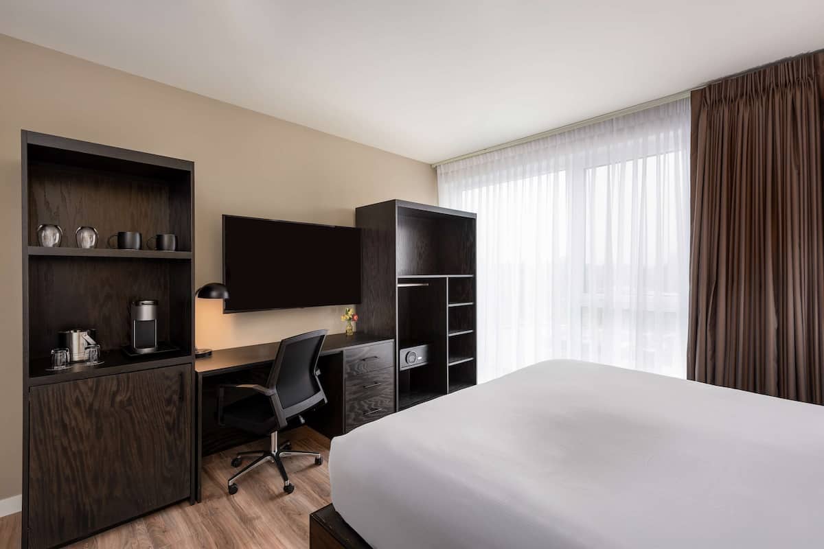 Ein Hotelzimmer mit Bett, Schreibtisch mit Stuhl, Fernseher und Einbauregalen mit Geschirr.