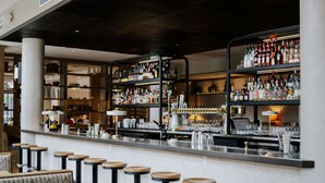 A bar area with multiple stools and shelves stocked with bottles. - Holman Riverfront Park Hotel Salem, Tapestry by Hilton (Salem)