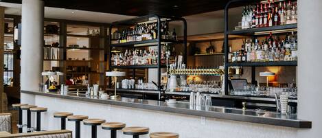 A bar area with multiple stools and shelves stocked with bottles.