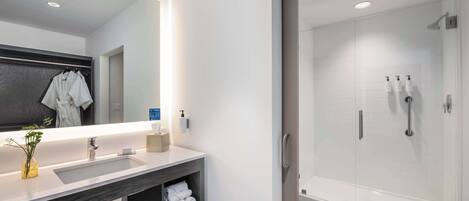 A modern bathroom with a large mirror, a sink, and a glass-enclosed shower.