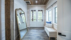 A room with a wooden ceiling, a large mirror, a white bench with pillows, and a door with glass panels. - Collins Creek 1 BR- Woodland Hills- 2 acres creek (Broken Bow)