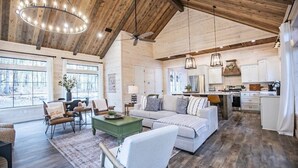 A spacious living area with a high ceiling, wooden beams, and a large window offering a view of the outdoors. - Collins Creek 1 BR- Woodland Hills- 2 acres creek (Broken Bow)