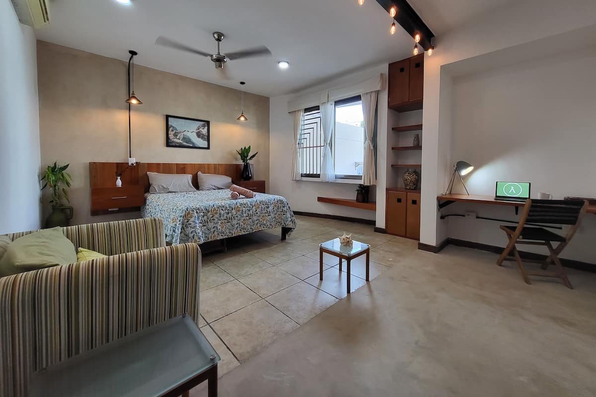 A modern hotel room with a bed, a sofa, a desk, and a small table.