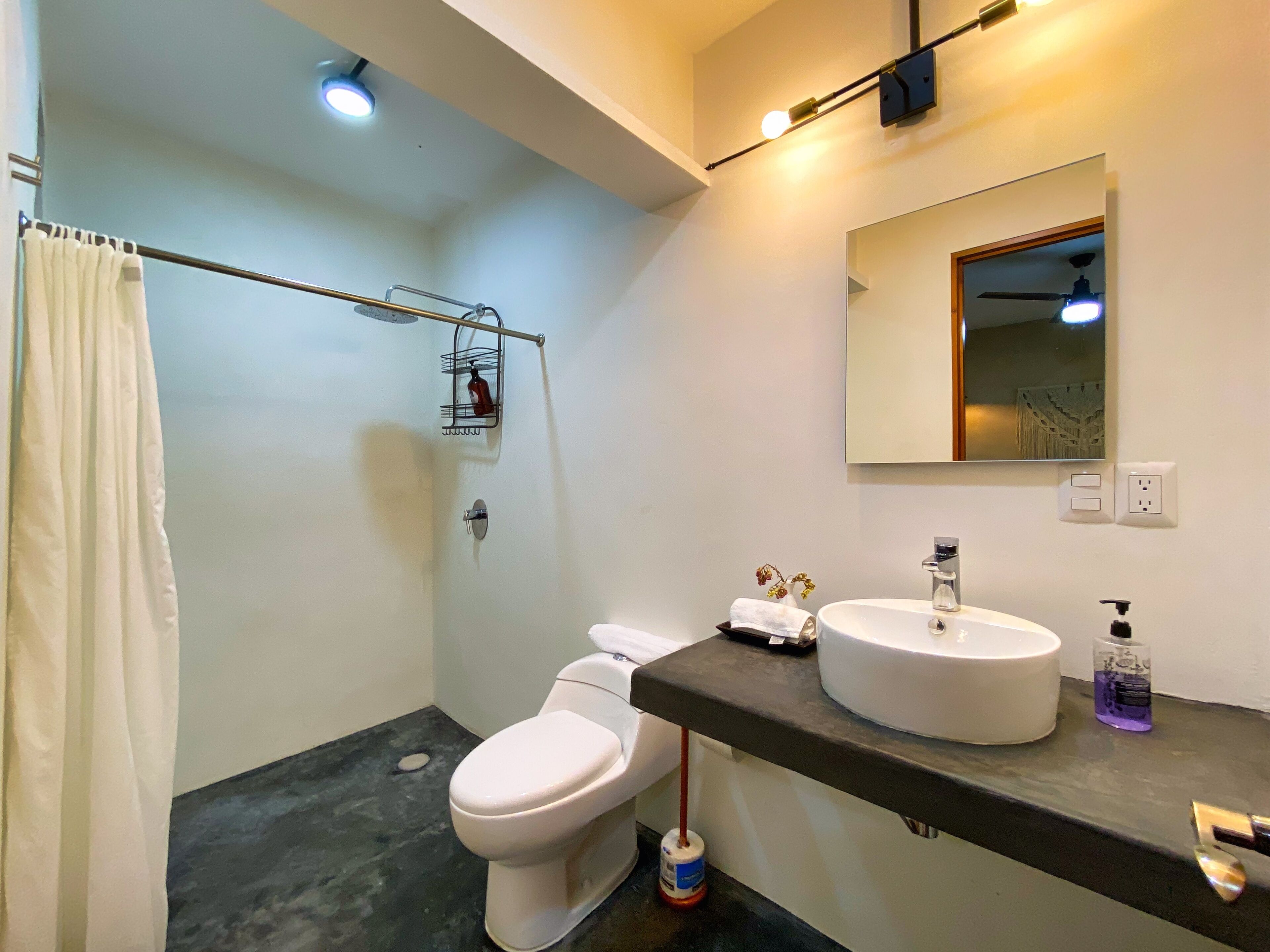 Un baño moderno con inodoro, lavamanos, espejo y ducha.