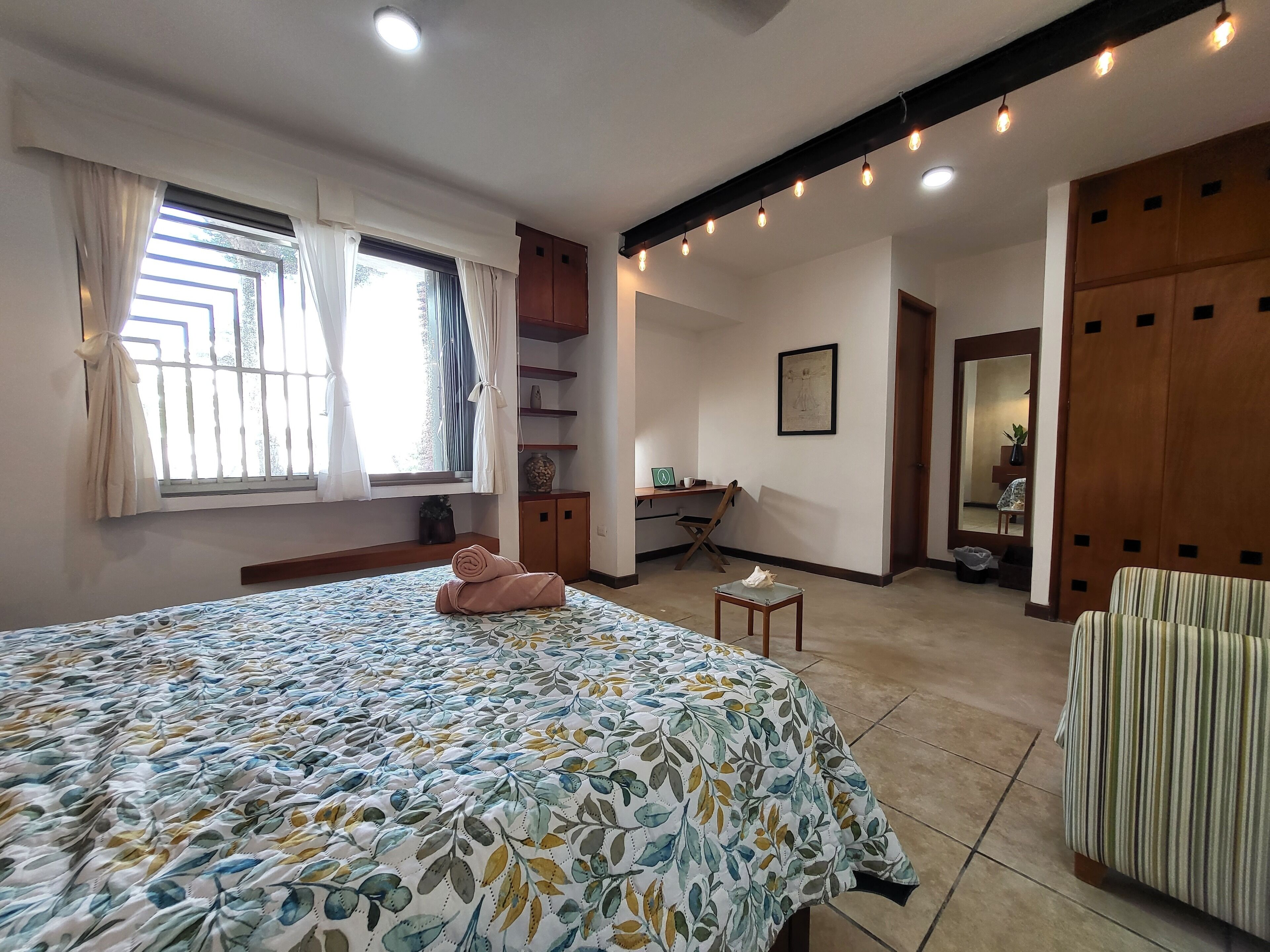 Une chambre à coucher comprenant un lit, un bureau, une chaise, une armoire et une fenêtre avec des rideaux.