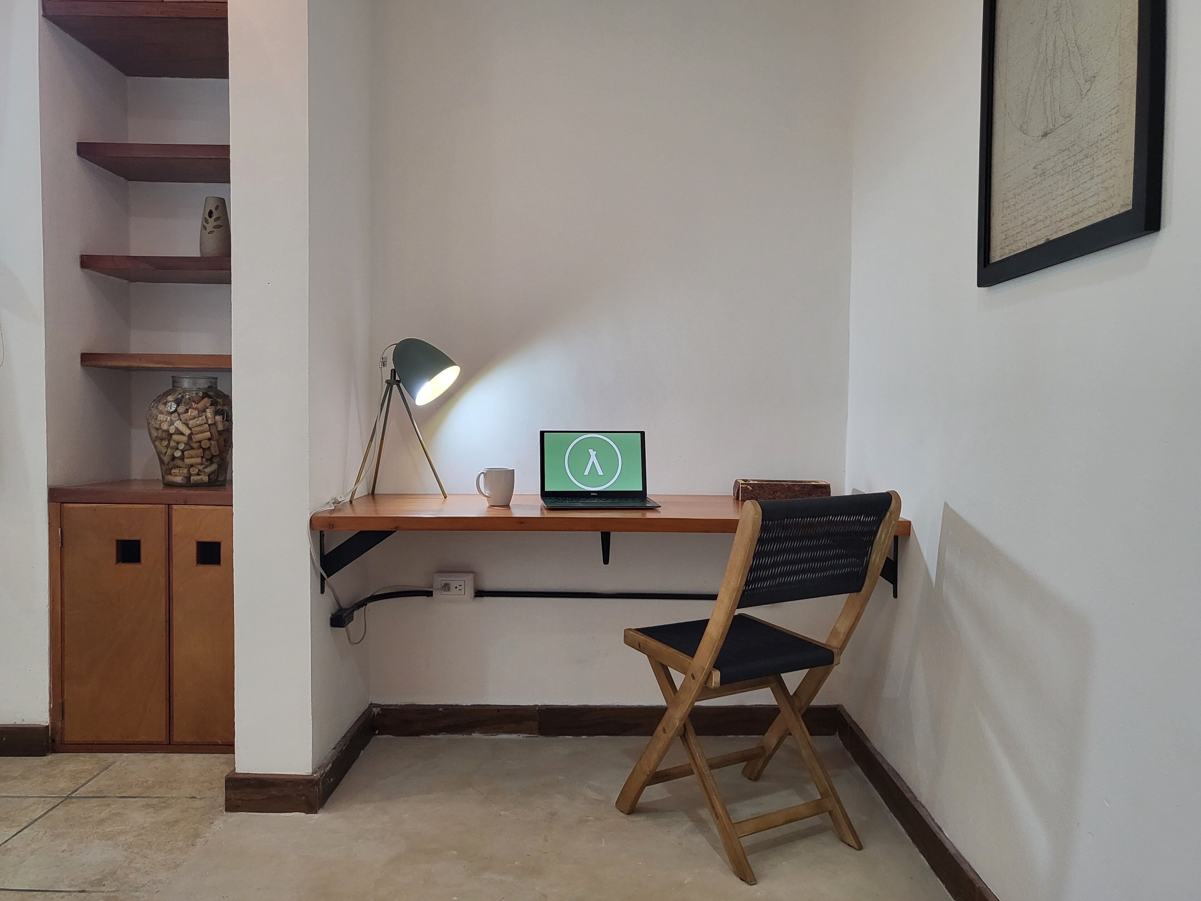 Un espacio de trabajo en esquina con escritorio, silla, lámpara, ordenador portátil y objetos decorativos.