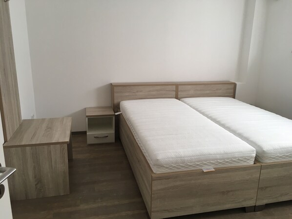 Une chambre à coucher avec un cadre de lit en bois, deux matelas blancs, une table de chevet en bois et un banc en bois.