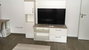 Et moderne værelse med et fladskærms-tv på et trætv-bord, hvide skabe og en dør.