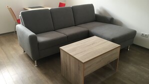En moderne stue med en grå hjørnesofa, et træbord og en rød lænestol.