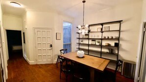 Uma sala de jantar com mesa de madeira, cadeiras, um candelabro e uma estante com objetos decorativos.