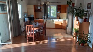 Une cuisine moderne avec des meubles en bois, une table à manger et des chaises. On y trouve également des plantes en pot et un réfrigérateur.