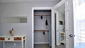 A room with a white vanity, a mirror, a small table with a decorative rooster, a closet with a hanging rack, and a door leading to another room. - ✪ King Beds ✔ 2 Bdr Townhouse w/ Private Backyard (Bryan)