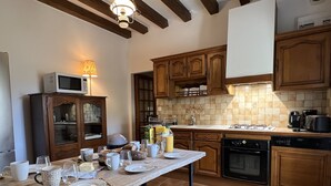 Una cocina con armarios de madera, salpicadero de azulejos, una mesa de comedor con platos, tazas y una lámpara.