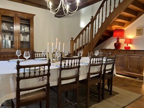 A dining area with a wooden table set for four, surrounded by chairs with intricate designs. A staircase with wooden railings and a chandelier is visible in the background. - Cosy house between Bordeaux and Saint-Emilion (beychac et cailleau)