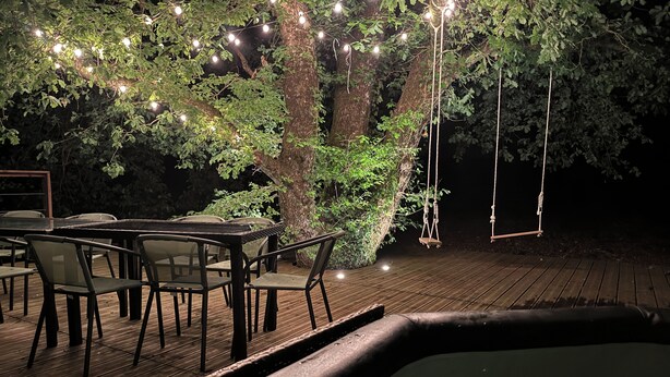 Terraza exterior con jacuzzi, mesas y sillas de madera, y luces colgantes.