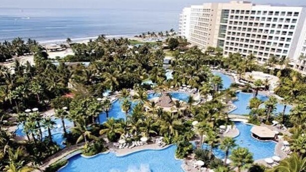 Ein Resort mit mehreren Swimmingpools, umgeben von üppiger Vegetation und Palmen, mit Blick auf den Ozean.