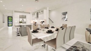 A modern dining area with a white table set for six, a kitchen in the background, and a view of the outdoors. - Luxury Paradise, walk to Las Olas -5 mins to Beach (Fort Lauderdale)