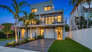 A modern two-story house with a garage, a well-maintained lawn, and a white fence. - Luxury Paradise, walk to Las Olas -5 mins to Beach (Fort Lauderdale)