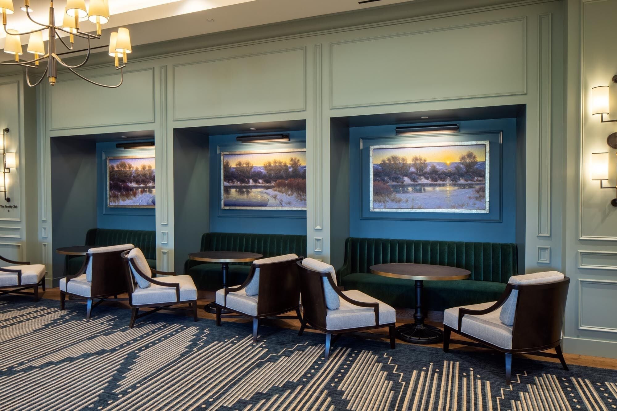 Un vestíbulo de hotel con una zona de estar que incluye sillones acolchados y mesas redondas, pinturas de paisajes enmarcados en las paredes, y una alfombra estampada.