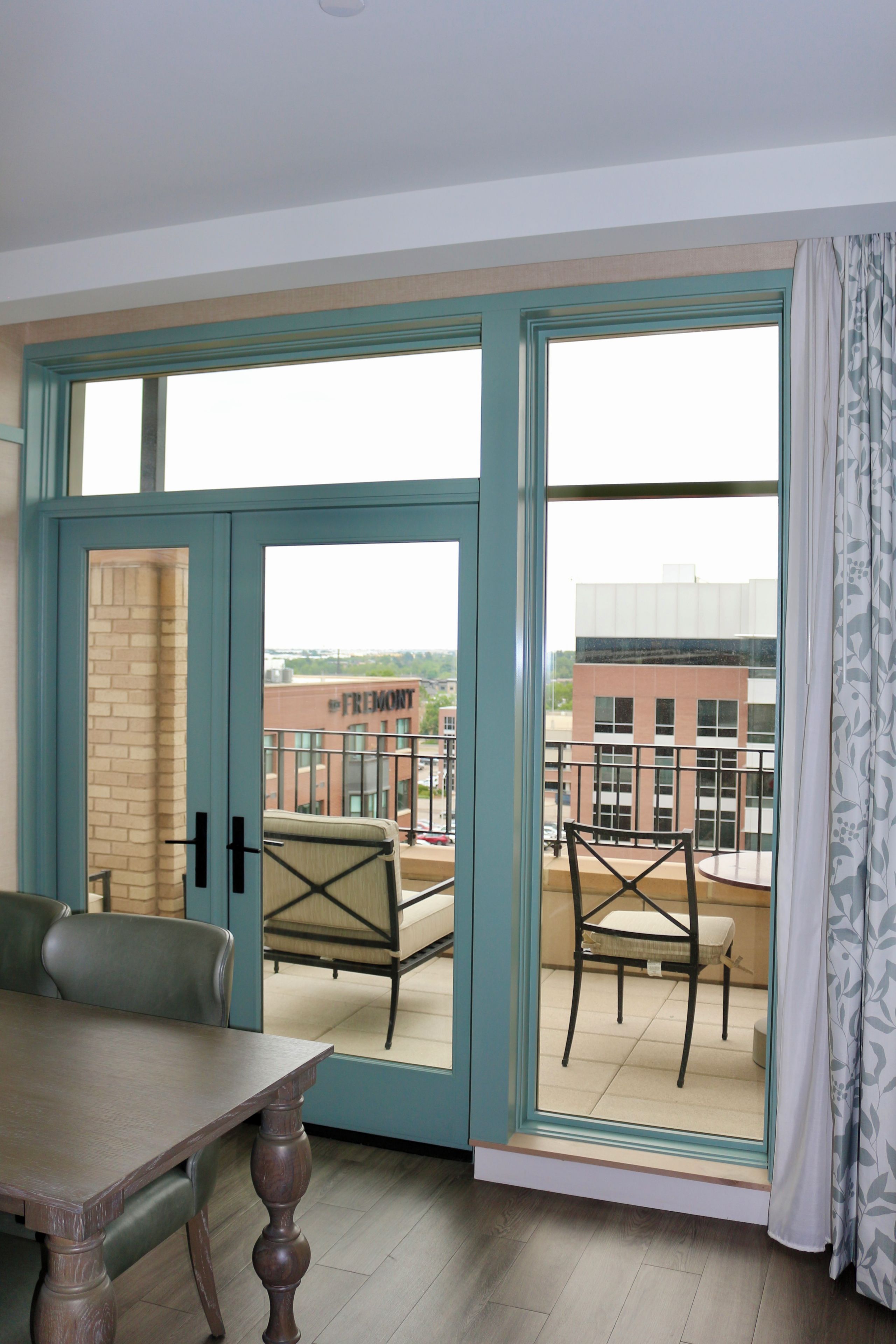 A room with a dining table, chairs, a sofa, and a balcony with a view of buildings.
