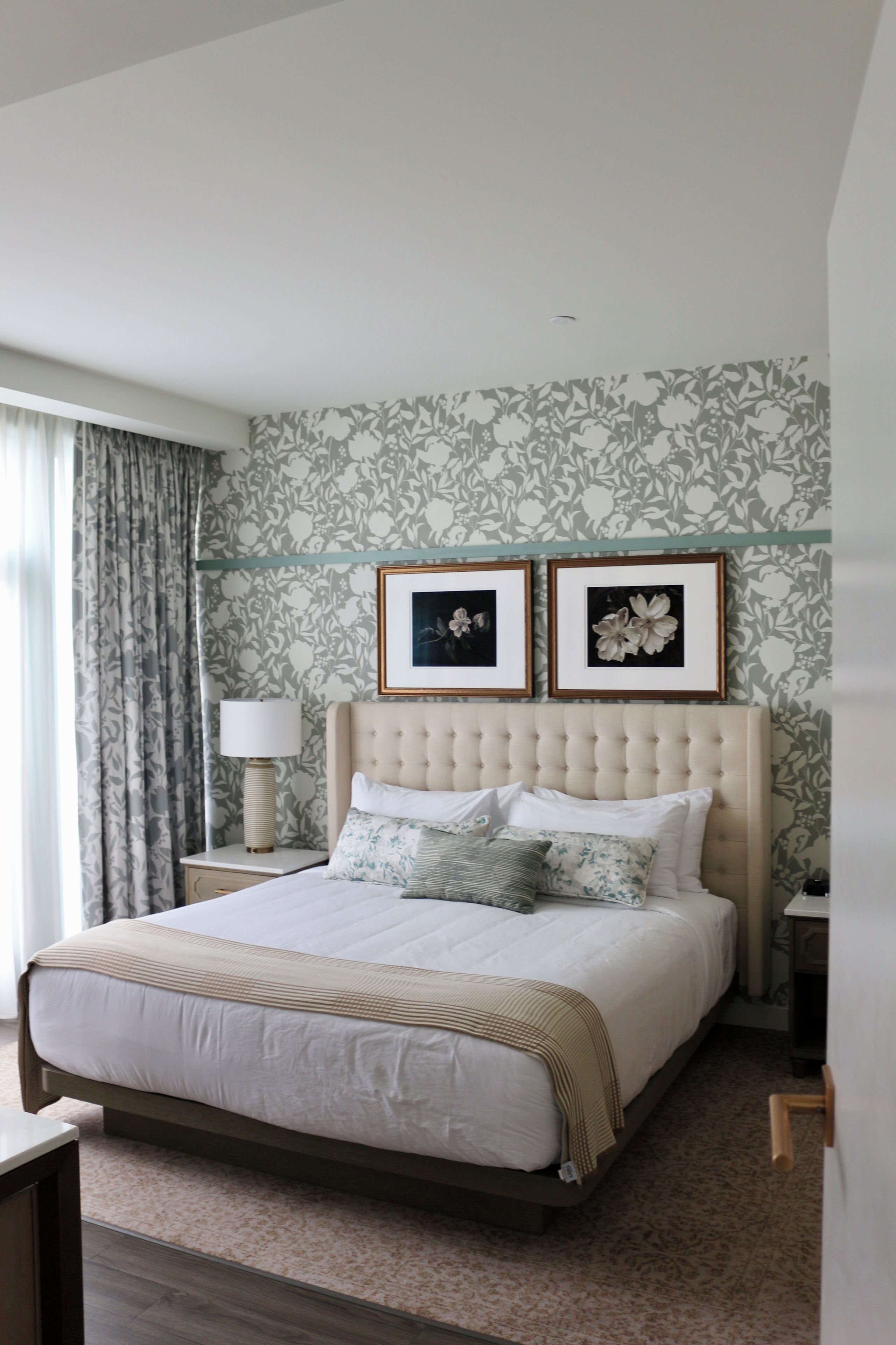 Une chambre d’hôtel avec un grand lit, une table de chevet, une lampe et deux tableaux encadrés au mur.