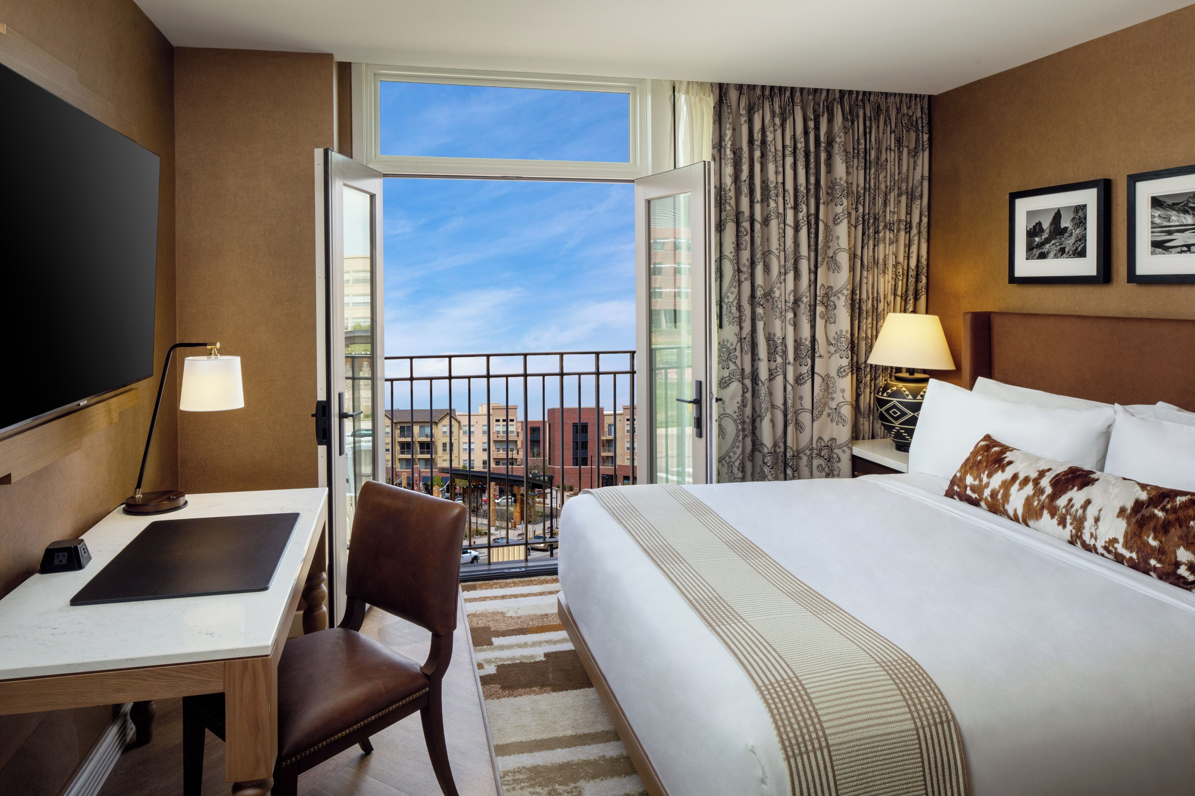 Une chambre d’hôtel équipée d’un lit, d’un bureau, d’une chaise, d’une télévision et offrant une vue sur le paysage urbain.
