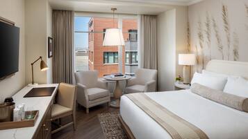 A hotel room with a bed, a desk, a chair, a small table, and a TV.