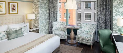 A hotel room with a large bed, two armchairs, a small table, and a desk with a lamp.