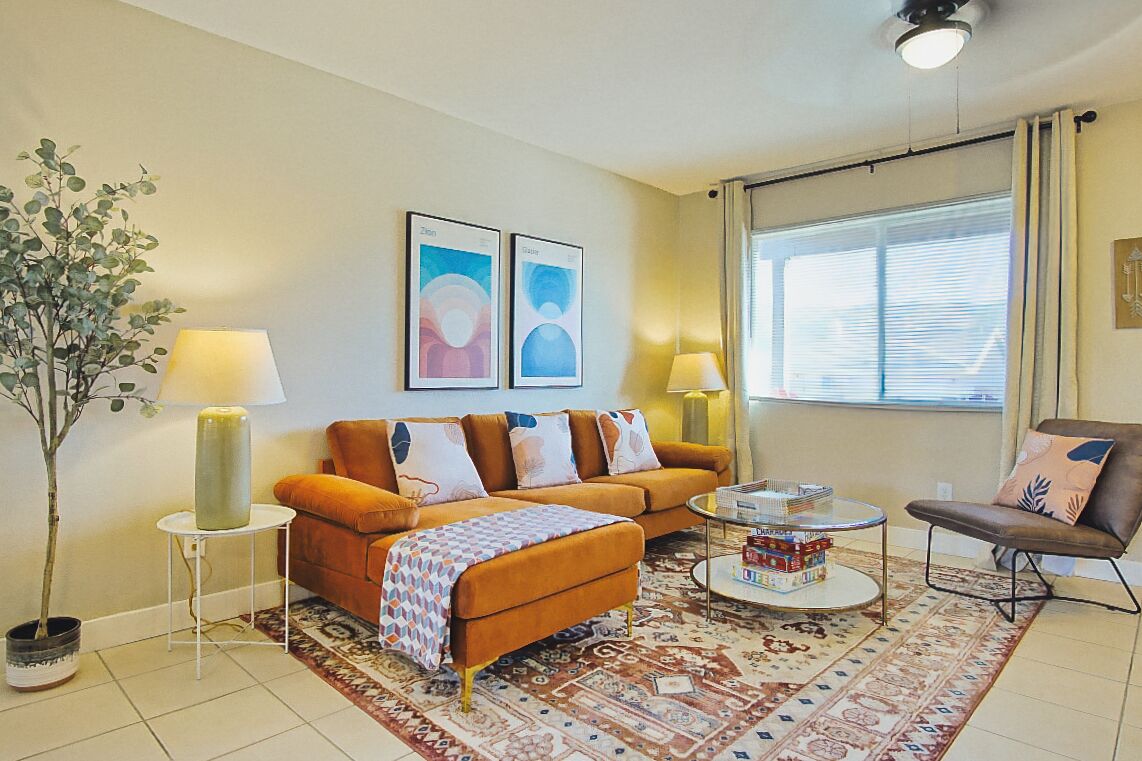 A living room with a sofa, two side tables, a coffee table, a chair, a lamp, a potted plant, and two framed pictures on the wall.