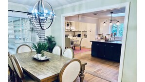 A dining area with a wooden table and chairs, a chandelier, and a view into the kitchen.