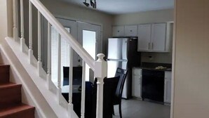 Cocina con gabinetes blancos, un refrigerador y un lavavajillas. Se ve una escalera con barandillas blancas que conduce a otra habitación.