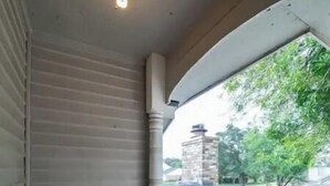 Un porche cubierto con vista a una calle residencial, una chimenea de piedra y una lámpara en el techo.