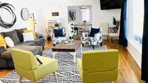 Un salon moderne avec un canapé gris, deux fauteuils jaunes, une table basse et, au fond, un coin repas.